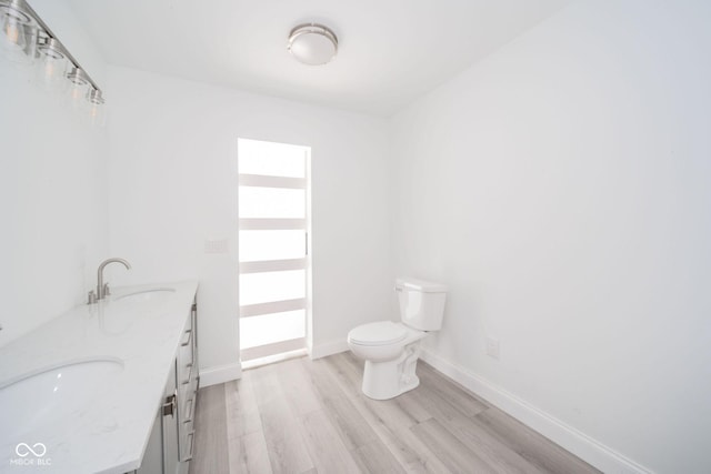 bathroom with a sink, double vanity, toilet, baseboards, and wood finished floors
