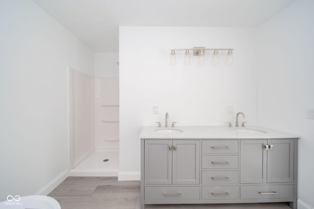 bathroom with baseboards, a sink, walk in shower, and wood finished floors