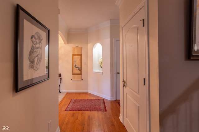 hallway with light wood-type flooring, ornamental molding, arched walkways, and baseboards