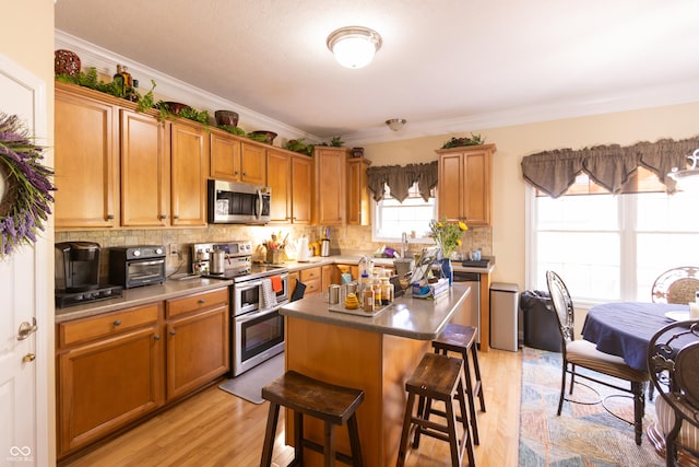kitchen featuring decorative backsplash, light wood-style floors, a breakfast bar area, ornamental molding, and appliances with stainless steel finishes