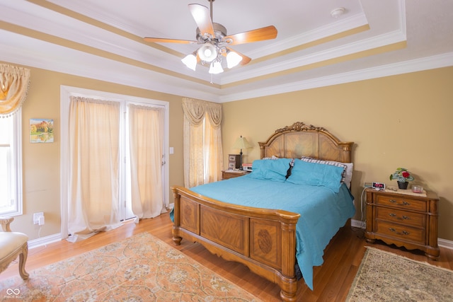 bedroom with light wood-style floors, crown molding, a tray ceiling, and a ceiling fan