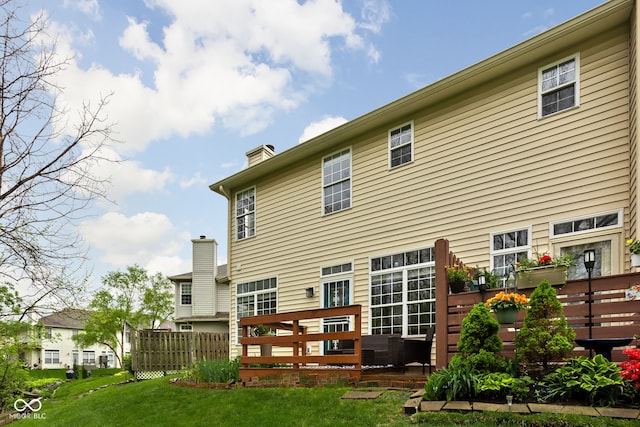 rear view of property with a lawn, a wooden deck, fence, and a chimney