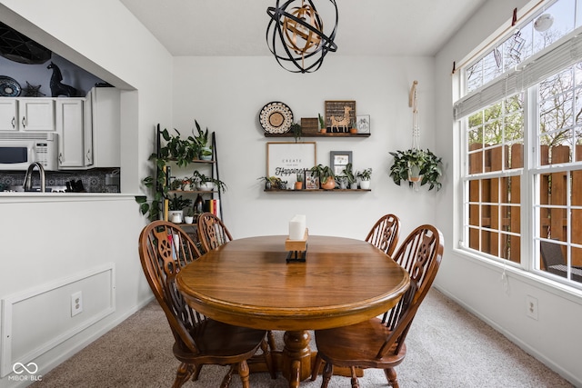 carpeted dining space featuring baseboards, a sink, and a chandelier