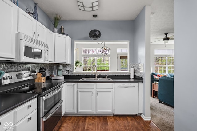 kitchen with white cabinets, dark countertops, a sink, white appliances, and backsplash