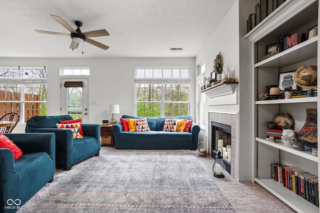 carpeted living room featuring a textured ceiling, a ceiling fan, a tile fireplace, and visible vents