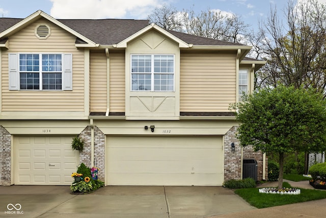 multi unit property featuring central AC unit, an attached garage, concrete driveway, and brick siding