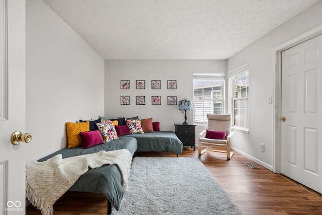 bedroom with visible vents, baseboards, a textured ceiling, and wood finished floors