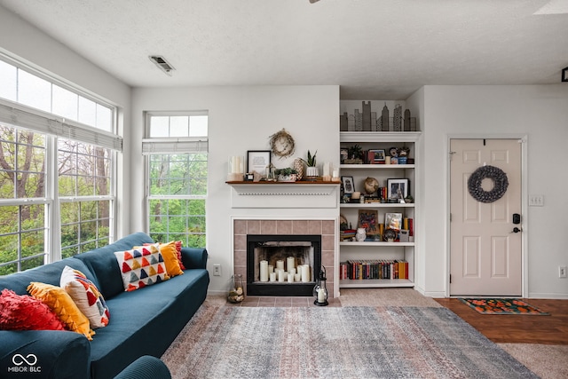 living room featuring a textured ceiling, baseboards, a tile fireplace, and visible vents