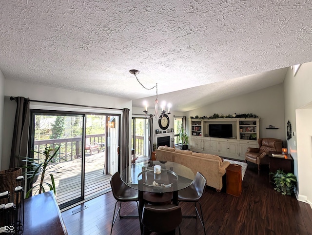 dining area featuring a textured ceiling, a fireplace, vaulted ceiling, an inviting chandelier, and dark wood-type flooring