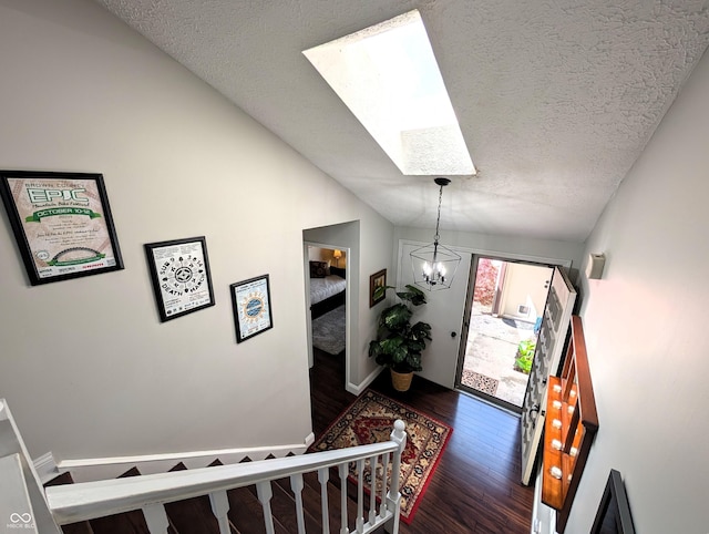 foyer entrance featuring vaulted ceiling with skylight, a textured ceiling, baseboards, dark wood-style floors, and a chandelier