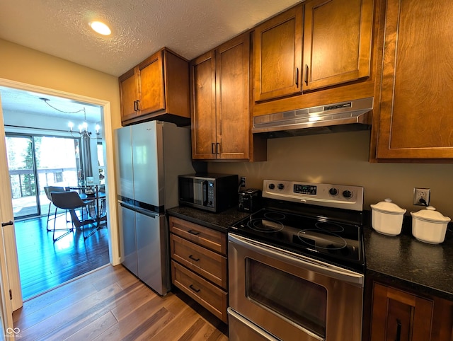 kitchen with brown cabinetry, a textured ceiling, appliances with stainless steel finishes, under cabinet range hood, and light wood-style flooring