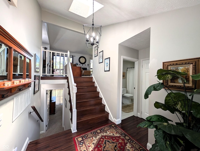 stairway with an inviting chandelier, baseboards, a skylight, and wood finished floors