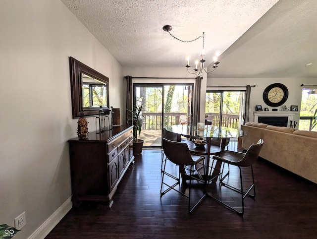 dining room featuring an inviting chandelier, a fireplace, a textured ceiling, dark wood finished floors, and baseboards