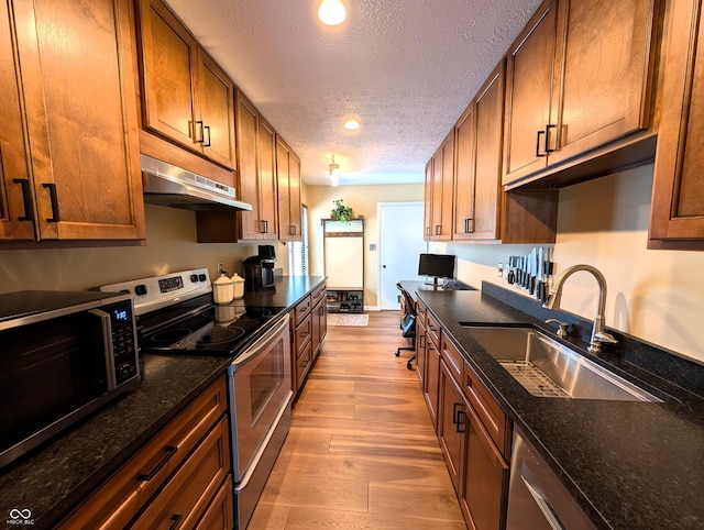 kitchen with a textured ceiling, wood finished floors, a sink, under cabinet range hood, and stainless steel appliances