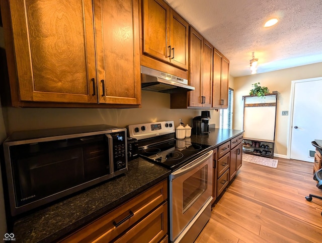 kitchen with a textured ceiling, brown cabinets, light wood finished floors, under cabinet range hood, and stainless steel appliances