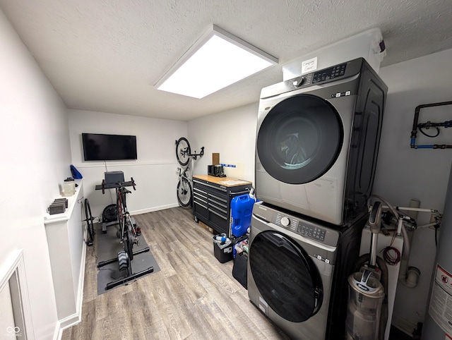 laundry room featuring laundry area, a textured ceiling, wood finished floors, baseboards, and stacked washer and clothes dryer