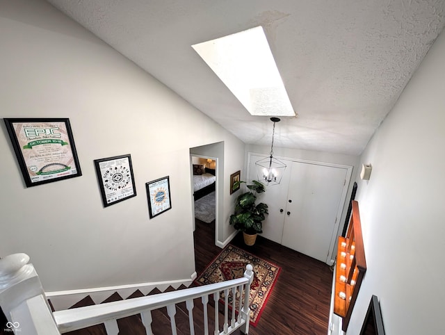staircase featuring an inviting chandelier, wood finished floors, baseboards, a textured ceiling, and a skylight