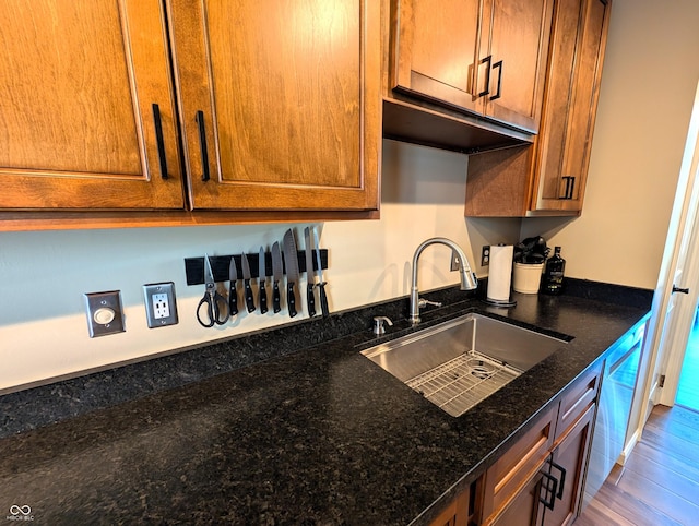 kitchen featuring a sink, dark stone counters, brown cabinetry, and wood finished floors