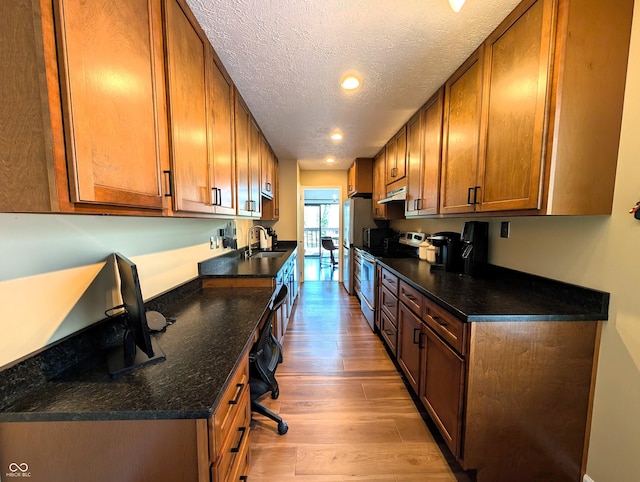 kitchen with appliances with stainless steel finishes, brown cabinets, light wood-type flooring, a sink, and under cabinet range hood