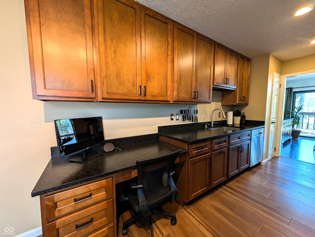 kitchen with built in desk, a sink, a textured ceiling, dark wood finished floors, and stainless steel dishwasher