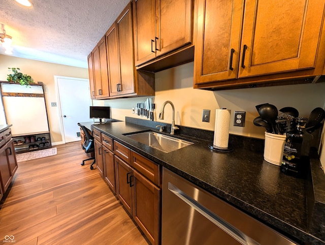 kitchen with a textured ceiling, brown cabinets, wood finished floors, dishwasher, and a sink