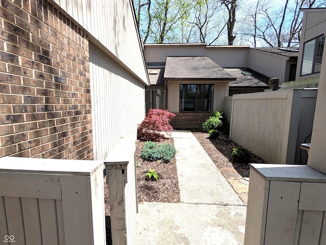 entrance to property featuring brick siding, roof with shingles, and fence