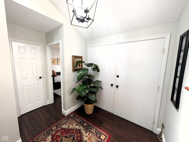 foyer entrance featuring baseboards, a textured ceiling, dark wood-style floors, and an inviting chandelier