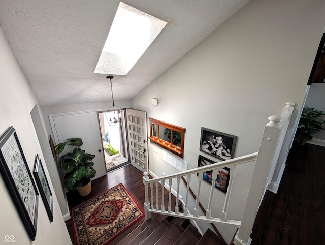 foyer with a textured ceiling, a chandelier, baseboards, wood finished floors, and lofted ceiling with skylight
