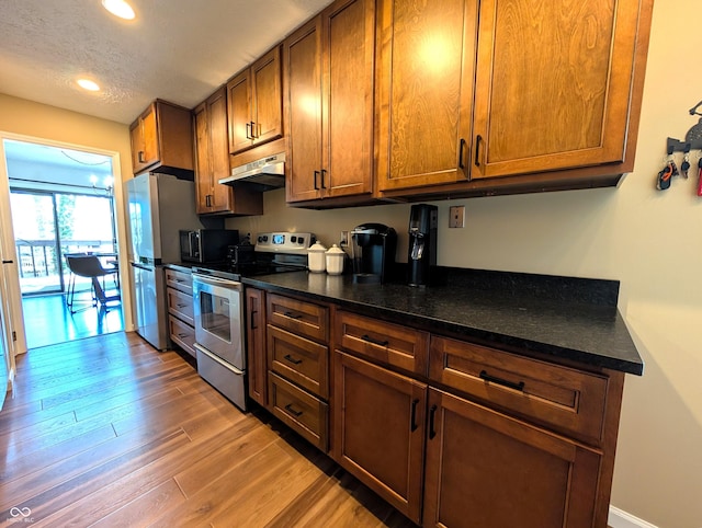 kitchen with brown cabinets, appliances with stainless steel finishes, recessed lighting, wood finished floors, and under cabinet range hood