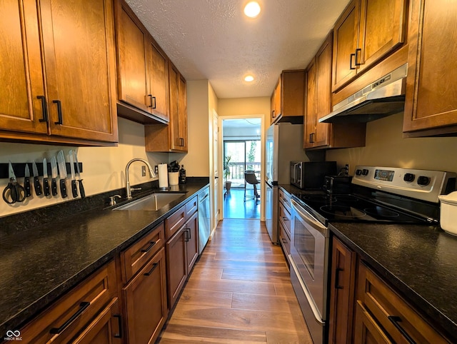 kitchen with wood finished floors, a textured ceiling, under cabinet range hood, a sink, and appliances with stainless steel finishes