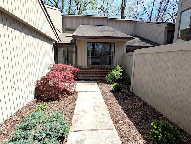 entrance to property with fence, a shingled roof, and brick siding