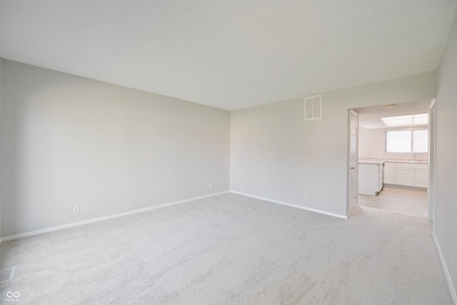 spare room with light carpet, a sink, visible vents, and baseboards
