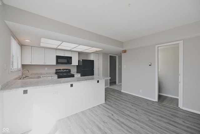 kitchen with a sink, black appliances, baseboards, light wood-style flooring, and a peninsula