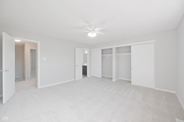 unfurnished bedroom featuring light carpet, a ceiling fan, multiple closets, and baseboards