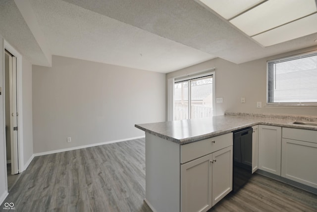 kitchen with wood finished floors, a sink, light countertops, a peninsula, and black dishwasher