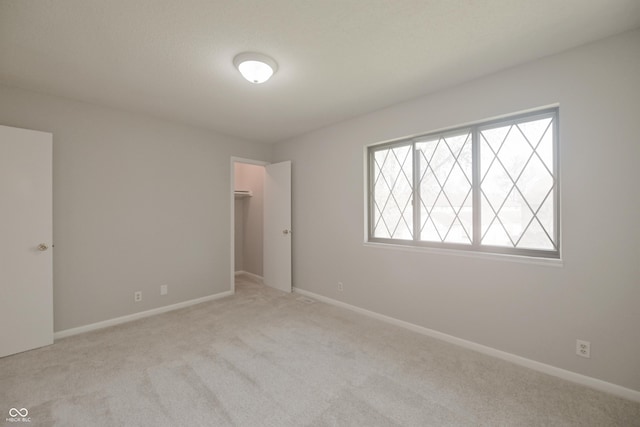 unfurnished bedroom featuring a walk in closet, light carpet, a closet, and baseboards