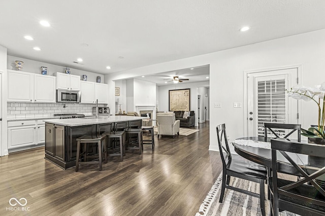 kitchen featuring a kitchen island with sink, a breakfast bar, recessed lighting, white cabinetry, and stainless steel microwave