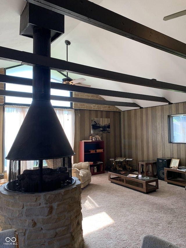 living area featuring carpet floors, a wood stove, wood walls, beam ceiling, and a ceiling fan