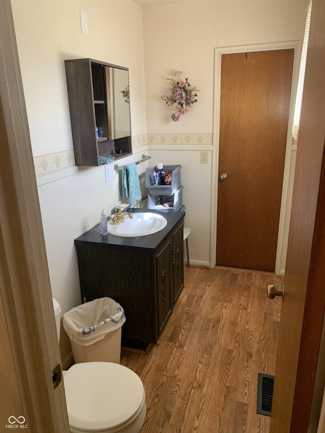 half bathroom with visible vents, wood finished floors, toilet, and vanity