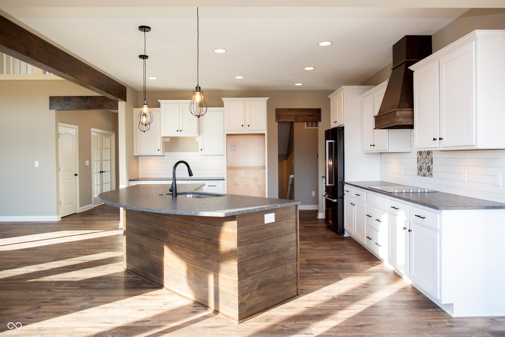 kitchen featuring a kitchen island with sink, high end black refrigerator, baseboards, tasteful backsplash, and a sink