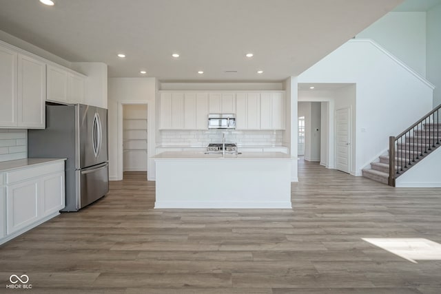 kitchen with white cabinets, stainless steel appliances, decorative backsplash, and light wood-type flooring
