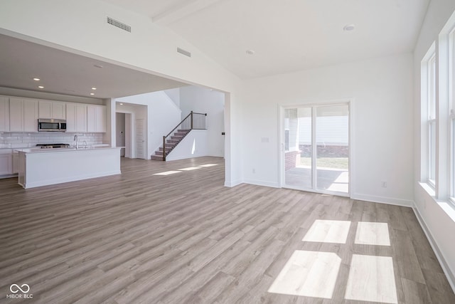 unfurnished living room with stairway, light wood-style floors, visible vents, and plenty of natural light