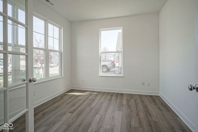 spare room with wood finished floors, a wealth of natural light, baseboards, and visible vents