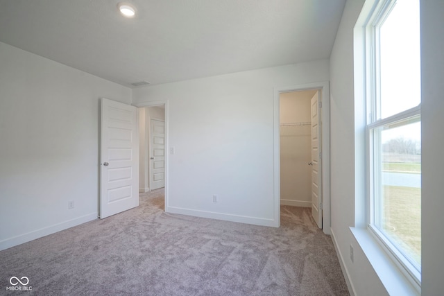 unfurnished bedroom with a walk in closet, carpet, and baseboards