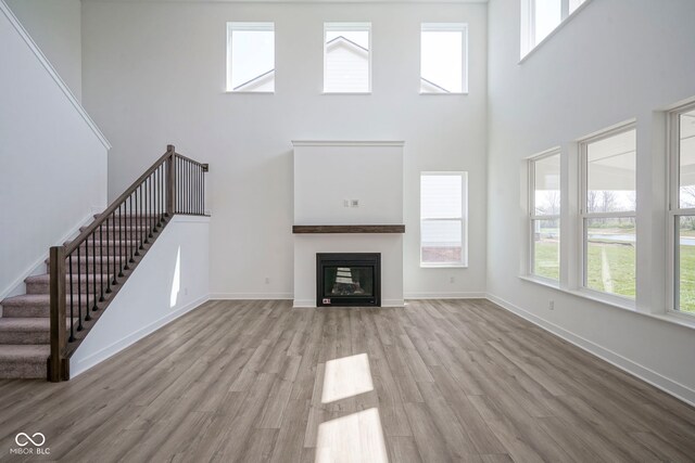 unfurnished living room with baseboards, a glass covered fireplace, a towering ceiling, wood finished floors, and stairway