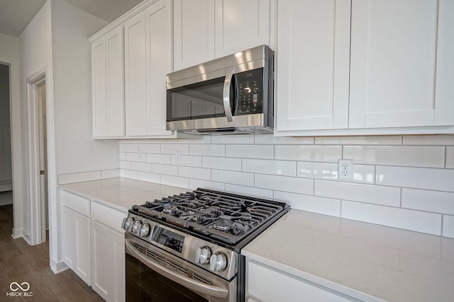 kitchen with light stone counters, tasteful backsplash, stainless steel appliances, white cabinetry, and dark wood-style floors