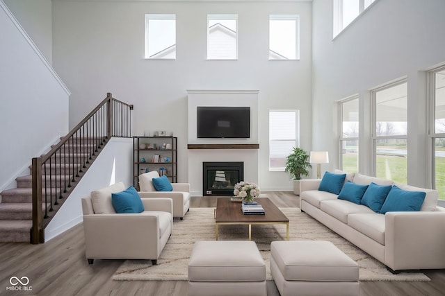 living area featuring wood finished floors, stairs, a glass covered fireplace, baseboards, and a high ceiling