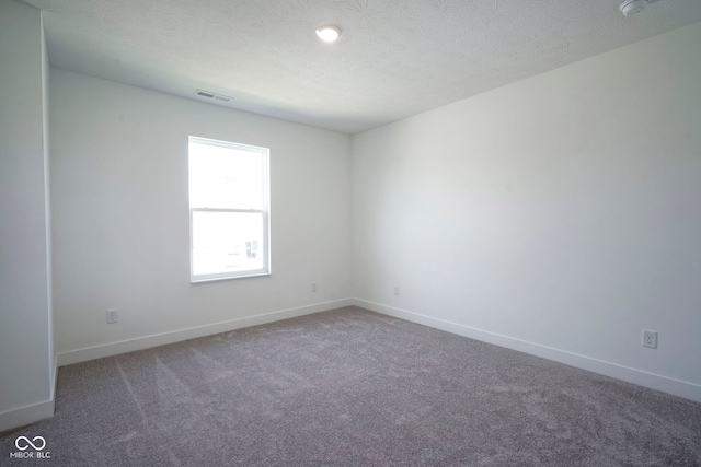 spare room with a textured ceiling, carpet floors, visible vents, and baseboards