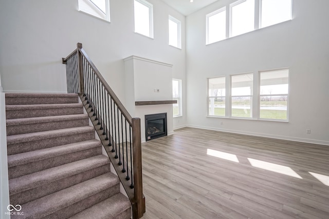 unfurnished living room with stairway, a high ceiling, wood finished floors, baseboards, and a glass covered fireplace