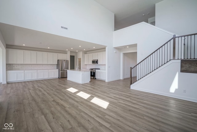 unfurnished living room featuring baseboards, a towering ceiling, light wood-style floors, visible vents, and stairs